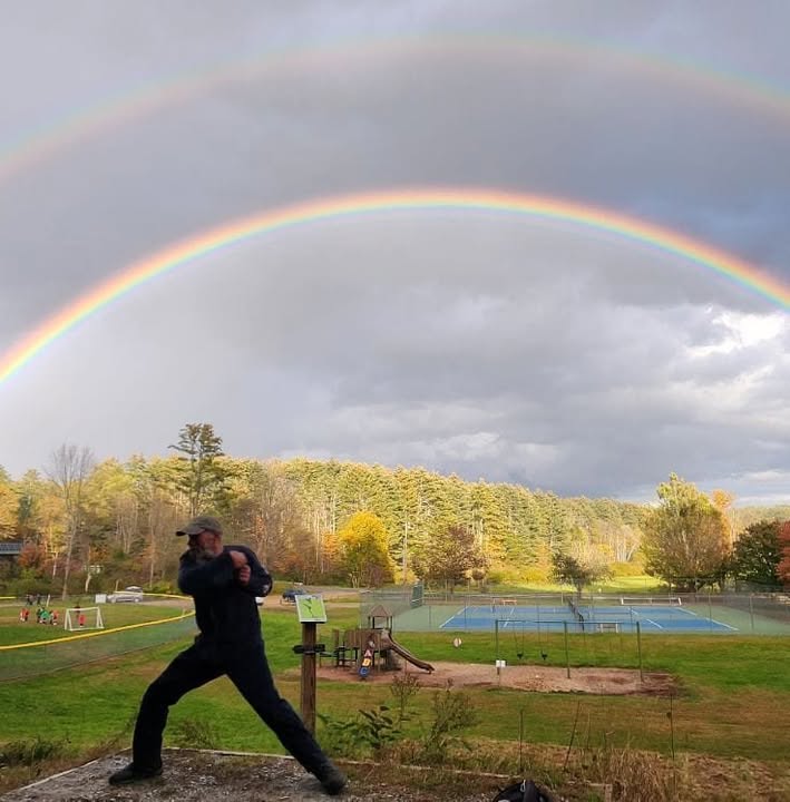 A disc golfer throwing from a tee beneath a double rainbow at Pinnacle Recreation Area