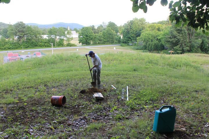 Volunteer installing a basket sleeve at the edge of a fairway